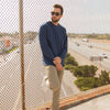 A man stands on a bridge in a navy blue crew neck sweater.