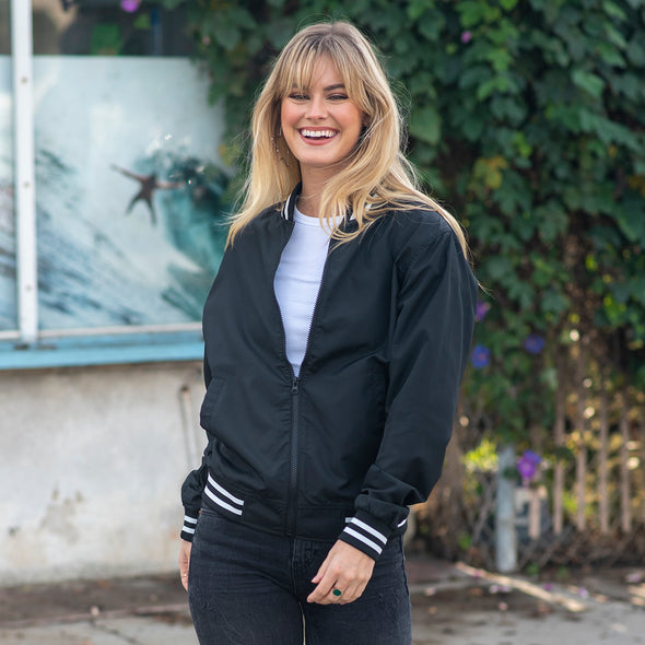 A woman is posing while wearing a black and white bomber jacket.