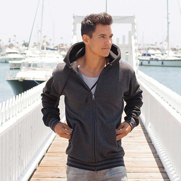Man poses on boardwalk in a varsity style hoodie.