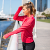 Woman looks away and is wearing a coral pink yoga jacket.