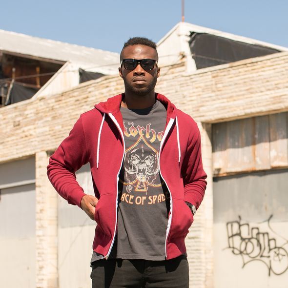 A man poses in a t-shirt and an unzipped burgundy hoodie.