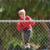 A boy is climbing a fence and he is wearing a red hoodie.