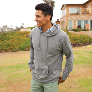 A man poses on grass while wearing a light gray jersey hoodie.
