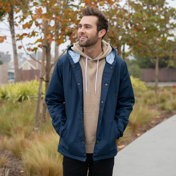 Man poses in a navy blue coach's jacket over a tan hoodie.