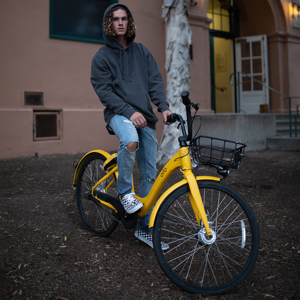 Man poses on a bike in a gray pullover hoodie.